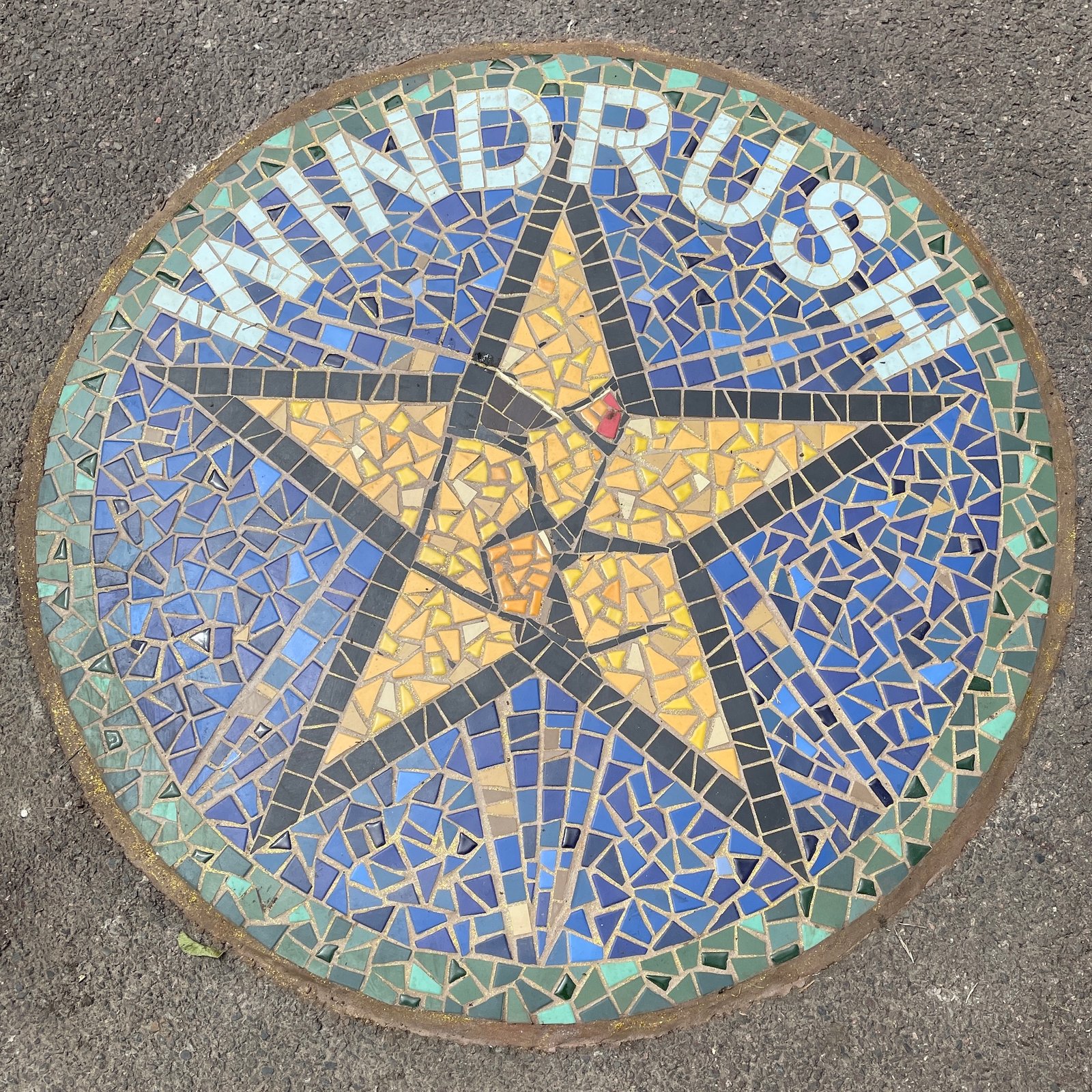 Circular Windrush mosaic star in the pavement, with a gold star and raised fist at the centre.